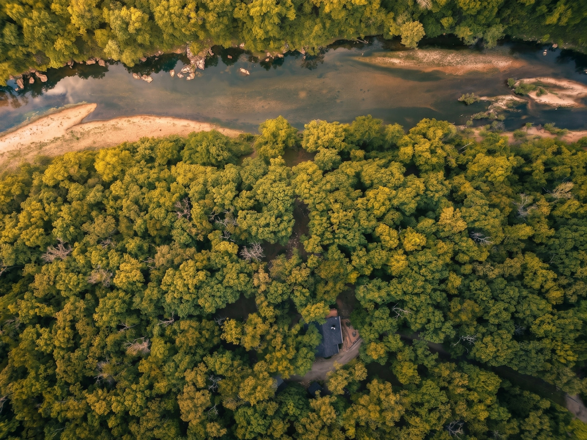 Aerial view of a river cabin tucked into Ozark forest at golden hour